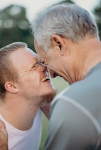 intergenerational picture of young adult and older man, heads together and big smiles on their face.