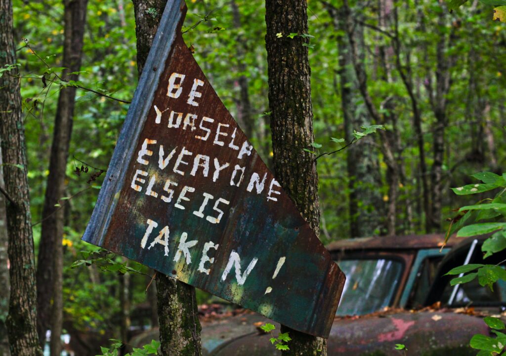 a rusty sign hand painted with the words "Be yourself, everyone else is taken"