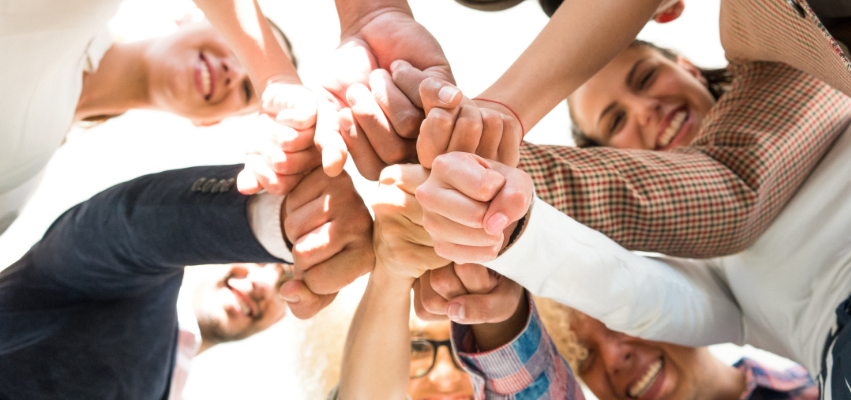 A team of adults put their hands into a huddle.