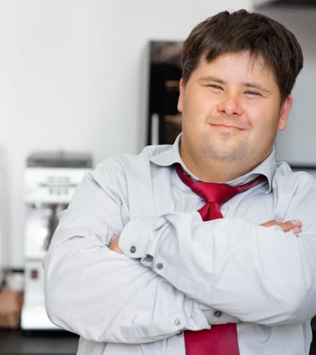 individual smiling at the camera with their arms crossed over. Standing in front of a coffee machine and smiling.